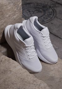 Paire de baskets blanches à lacets reposant sur des marches en pierre près d'une plaque d'égout métallique ronde sur une surface pavée.