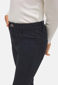 Pantalones negros de corte slim, con trabillas para cinturón, bolsillos frontales y una suave mezcla de algodón. Presentan un cierre de botón metálico.