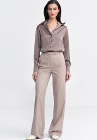 Jasnobrązowa satynowa bluzka z zapięciem na guziki i szerokim kołnierzem, w połączeniu z beżowymi spodniami w paski, z wysokim stanem i rozszerzającymi się nogawkami.