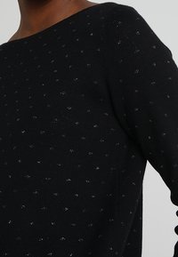 Maglione nero a maglia con un ampio scollo e macchie argentate in tutto. Texture liscia con maniche lunghe, aderente in vita.