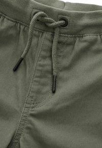 Olijfgroene shorts met een geribbelde tailleband, een trekkoordsluiting met zwarte plastic uiteinden en subtiele stikdetails op de stof.