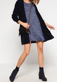 Granatowy dzianinowy kardigan na krótką, teksturowaną niebieską sukienkę. Czarna torebka na ramię z frędzlami. Czarne botki na klockowym obcasie.