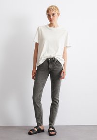 Svijetlosivi T-shirt, uske tamnosive traperice i crne sandale. Mekani materijal, ležeran kroj, jednostavan dizajn, s vidljivim šavovima na trapericama.
