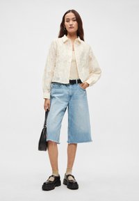 Kremowa, przezroczysta kurtka w kwiaty na beżowej bluzce, w połączeniu z jasnoniebieskimi dżinsowymi kulotami. Czarny pasek i buty, beżowe skarpetki oraz czarna torba.