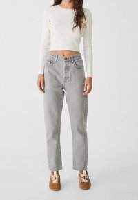 Jeans grises de tiro alto con un corte recto, combinados con una blusa ajustada de manga larga de canalé blanca y zapatillas de ante marrones.