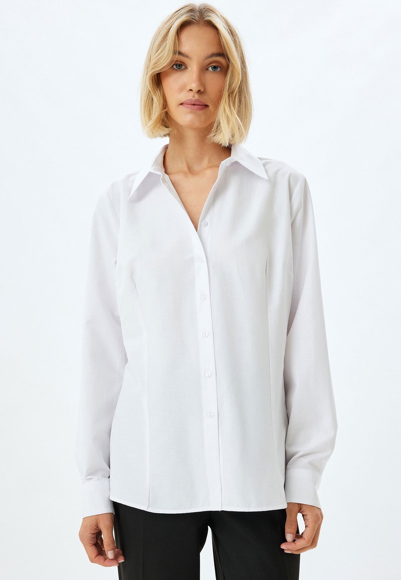 Vit långärmad skjorta med knapplåstning och krage, tillverkad av ett mjukt tyg, med rak passform och minimalistisk design.