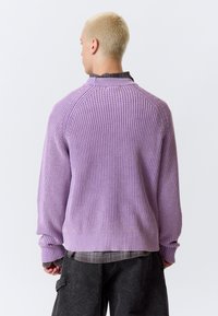 Pull en maille côtelée violet avec col montant et manches longues, présentant une texture contrastée et une coupe décontractée. Ourlet arrondi à la taille.