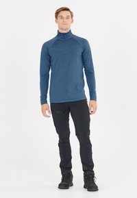 Maglia a maniche lunghe blu con zip a metà, dal texture liscia, con una cucitura sul petto. Abbinata a pantaloni neri aderenti e stivali neri robusti.