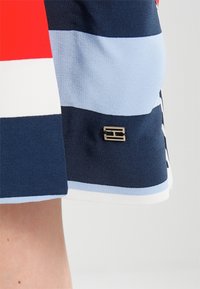 Falda de tela a rayas que presenta colores rojo, blanco, azul claro y marino. Incluye un pequeño acento metálico con el logo en el dobladillo.