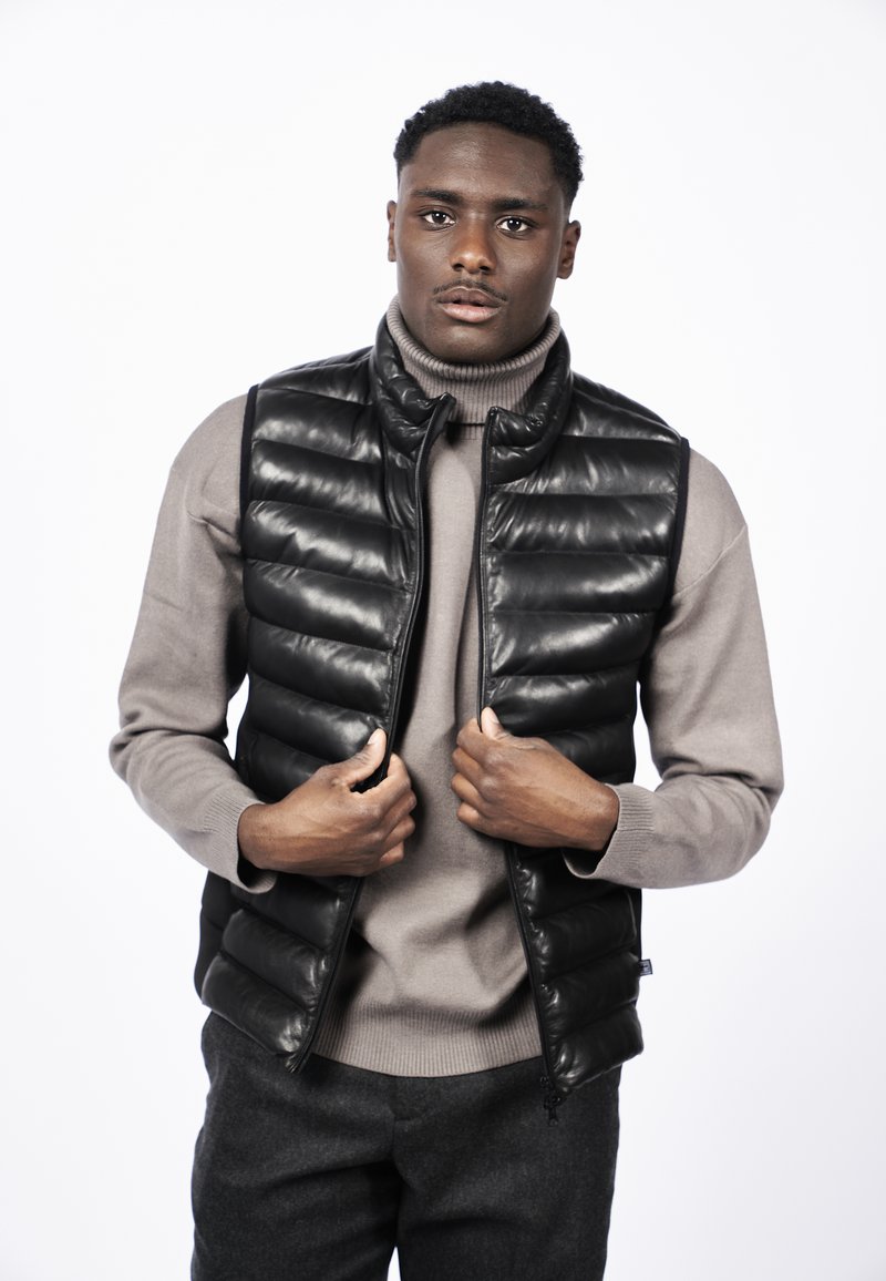 Mustapuffatakki, jossa on tikattu pintakuvio, varustettuna vetoketjukiinnityksellä, käytetty vaaleanharmaan poolopuseron päällä, yhdistettynä tummansävyisiin housuihin.