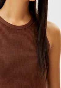 Débardeur marron à côtes avec un col rond, présentant une coupe ajustée et une texture lisse. Le tissu semble extensible, améliorant le confort.