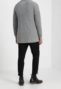 Maglione lungo grigio a coste con scollo rotondo. Indossato sopra pantaloni neri attillati e stivaletti neri. Finitura in maglia testurizzata.