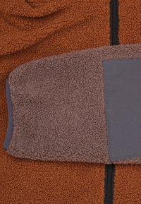 Bruine fleece stof met een gestructureerd oppervlak, gecombineerd met een grijs, glad stofdeel. Ritsdetail in het midden.