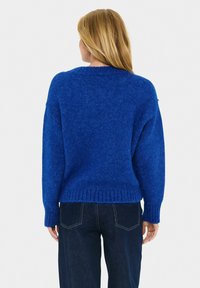 Blauwe gebreide trui met een losse pasvorm, ronde halslijn en geribde zoom. Zachte textuur met een iets fuzzy uitstraling. Gecombineerd met donkere jeans.