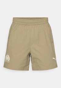 Μπεζ αθλητικά σορτς με ελαστική μέση, πλαϊνές τσέπες και τυπωμένα λογότυπα συλλόγου και εμπορικο ύ σήματος στο μπροστινό μέρος.