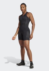 Black sleeveless bodysuit with a fitted design, textured panels, and three vertical stripes on each side. Worn with black athletic shoes.