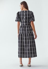 Mustvalge ruuduline midi-kleit puffvarrukatega, selja nuppudega ja kihilise seelikuosa, millel on hästi istuv bodice ja kogutud vöökoht.