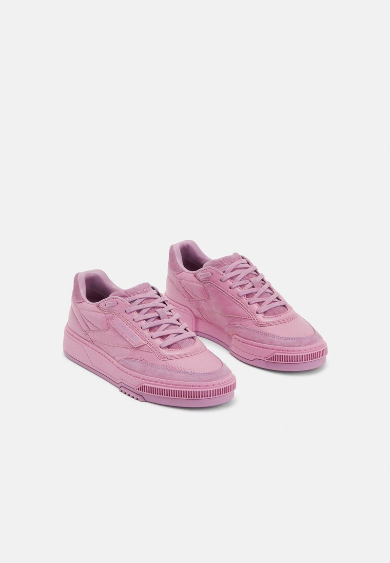 Pink sneakers featuring a smooth leather texture, low-top design, round toe, and flat rubber outsole with a patterned grip.