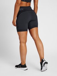 Svarta ribbade shorts med hög midja, med en strukturerad design och reflekterande logotyp; matchade med svarta sportskor.