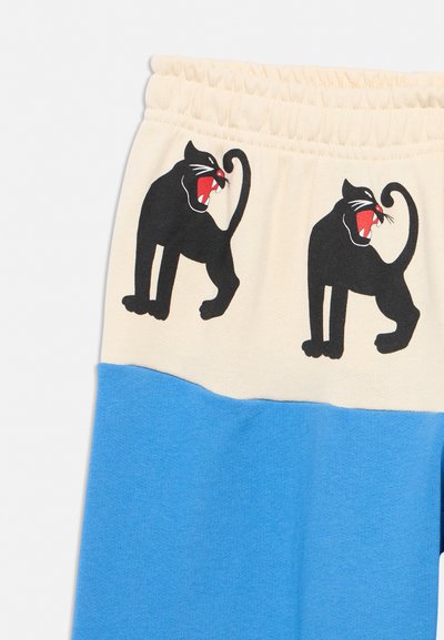Cotton pants with elastic waistband, cream upper part featuring two snarling black panther prints, and bright blue lower part.