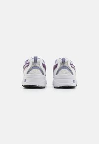 White athletic shoes with a mesh upper, purple accents, round toe, and cushioned soles. Features dual pull tabs at the heel for easy wear.