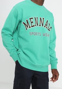 Felpa verde menta con collo a giro, con la scritta "MENNAZE SPORTS WEAR" in colori a contrasto. Tessuto morbido, con polsini e fondo a costine.