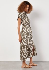 Khaki- und weißes gemustertes Hemdkleid mit kurzen Ärmeln, tailliertem Bund, Knopfleiste und seitlichem Schlitz. Kombiniert mit beigen flachen Sandalen.