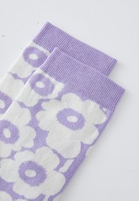 Calcetines morados y blancos con un patrón floral, de tejido de punto, con banda superior acanalada, presentan diseños de flores prominentes y una textura suave.