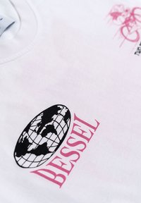 Camiseta de algodón blanca con un diseño de globo negro y texto "BESSEL" en rosa. La tela tiene una textura suave con costuras visibles.