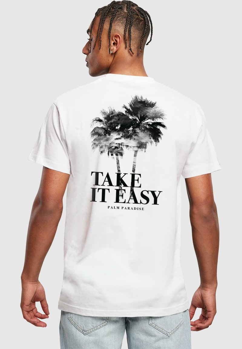 White cotton t-shirt featuring a black palm tree graphic and text "TAKE IT EASY PALM PARADISE" on the back. Short sleeves and relaxed fit.