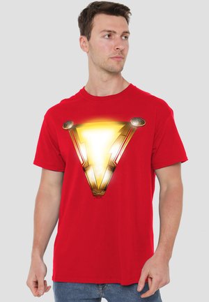 Young man wearing a red t-shirt with a glowing gold lightning bolt emblem, looking to the side against a plain background.