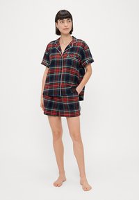 Red, blue, and green plaid short-sleeve pajama set with a button-up top and matching shorts. Features white piping and a chest pocket.