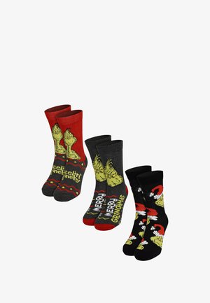Quattro paia di calzini alla caviglia in rosso e nero, con design del Grinch e testo. I materiali sembrano lavorati a maglia, con diversi motivi e colori.