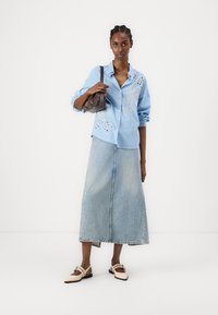 Camisa azul clara às riscas com bordado floral, combinada com uma saia jeans longa e sapatilhas de bico fino de cor clara. Pequena bolsa escura.