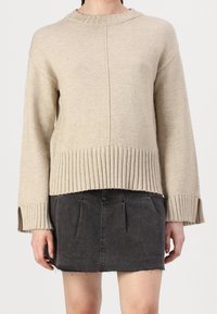 Beige stickad tröja med ribbad nederkant och ärm, med rund halsringning och rak skärning, tillsammans med en mörk denimkjol.