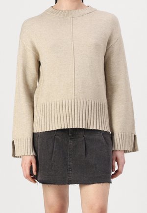 Beige gestrickter Pullover mit geripptem Saum und Bündchen, im Crew-Neck-Design und geradem Schnitt, kombiniert mit einem dunklen Denim-Rock.