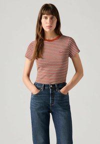 Camiseta de manga corta a rayas en naranja, blanco y azul. Cuello redondo con ribete rojo. Combinada con jeans de tiro alto en azul oscuro.