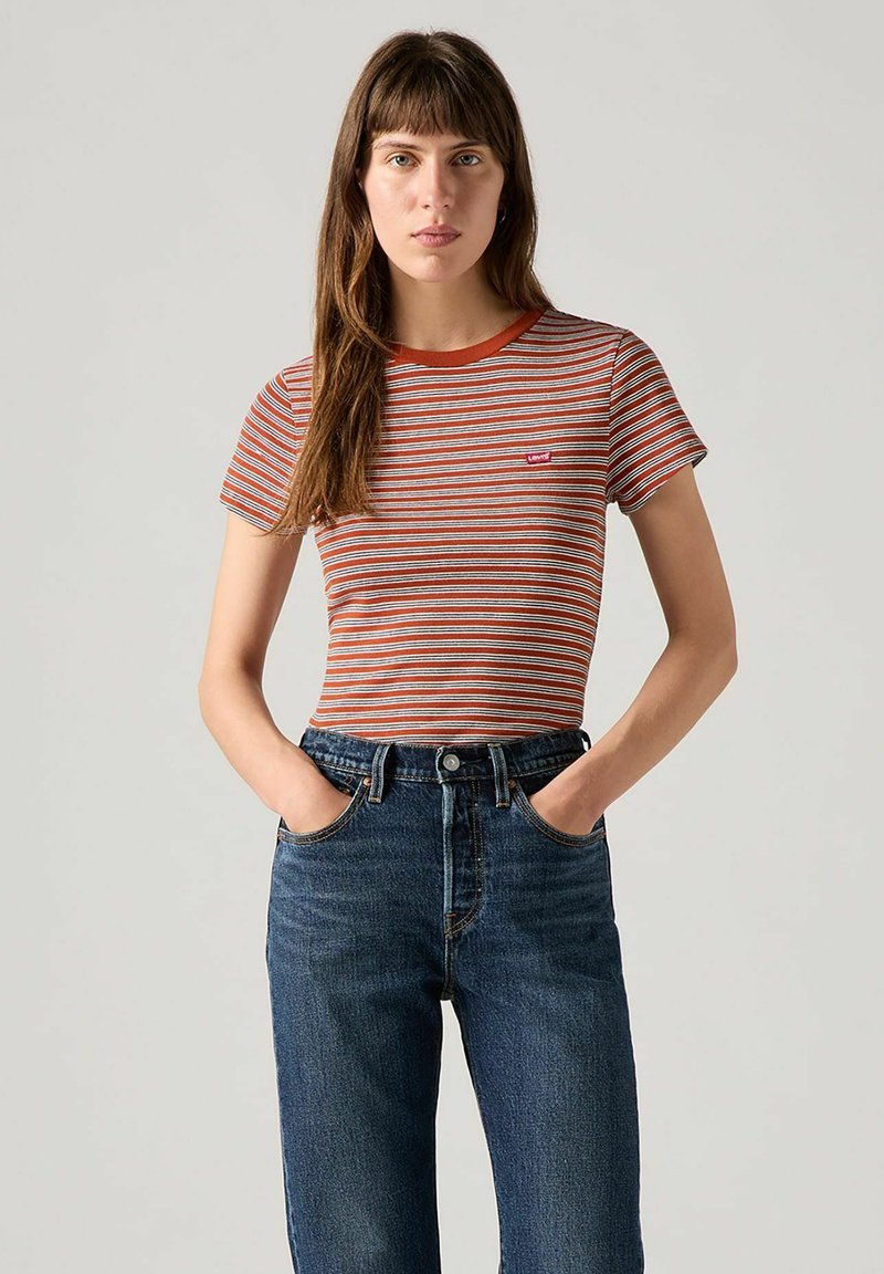 Camiseta de manga corta a rayas en naranja, blanco y azul. Cuello redondo con ribete rojo. Combinada con jeans de tiro alto en azul oscuro.
