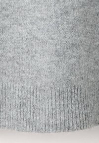 Gros plan d'un tissu tricoté doux gris clair avec une texture côtelée sur le bord inférieur, montrant des motifs de couture détaillés.