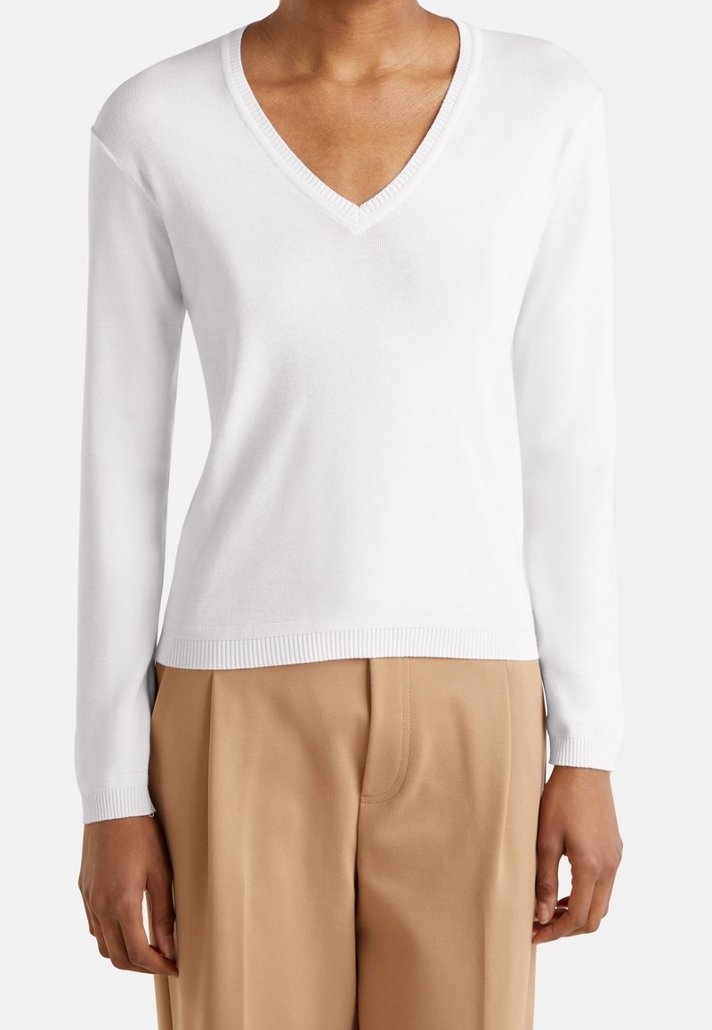 Biały sweter z długim rękawem i dekoltem w serek, z prążkowanymi mankietami i dolnym obszyciem, wykonany z miękkiego materiału, zestawiony z jasnobeżowymi, wysokim stanem spodniami.