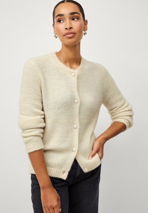 Cardigan lavorato a maglia beige chiaro con una texture morbida, scollatura rotonda e bottoni simili a perle. Presenta maniche lunghe e un'apertura frontale leggermente aperta.