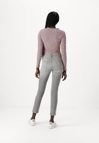 Lange mouwen, gestreept shirt in lichtroze en wit, gecombineerd met lichtgrijze, slim-fit jeans met achterzakken en een tan lederen logo label. Witte sneakers.