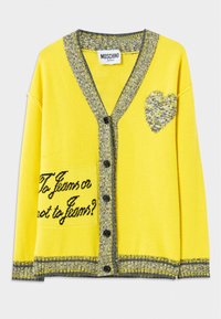 Gul stickad cardigan med grå detaljer, har ett hjärtmönster och texten "Att ha jeans eller inte ha jeans?" på vänster ficka. Sex svarta knappar.