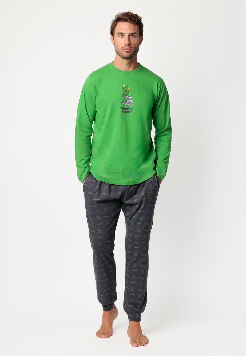 Camisa verde de manga larga con un gráfico de Kermit y texto, combinada con pantalones gris oscuro que presentan un patrón verde repetido. Material ligero.
