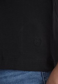 Svart bomull T-skjorte med rund hals og korte ermer. Har en liten svart brodert globuslogo ved kanten.