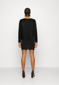 Top preto de mangas longas feito de tecido macio, combinado com uma saia mini preta ajustada, apresentando uma textura suave e um design simples.