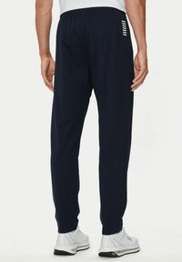 Pantaloni da jogging blu navy con vita elastica, dotati di dettagli a strisce bianche nella zona della tasca posteriore e tessuto dalla texture liscia.