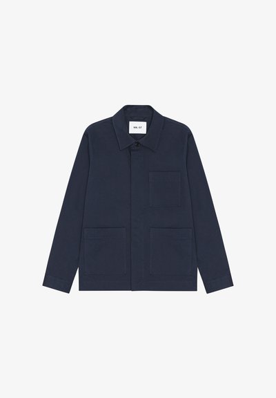 Camicia giacca blu navy a maniche lunghe con tre tasche frontali e colletto, abbottonata in alto, con etichetta NN.07 all'interno del colletto.