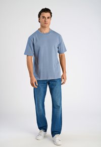 Jasnoniebieska bawełniana koszulka z okrągłym dekoltem i krótkimi rękawami, w połączeniu z niebieskimi dżinsami prostymi i białymi trampkami. Prosty design, swobodny krój.