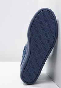 Niebieski sneaker z teksturowaną cholewką z tkaniny i gumową podeszwą. Podeszwa charakteryzuje się powtarzającym się wzorem logo oraz elementami geometrycznymi.